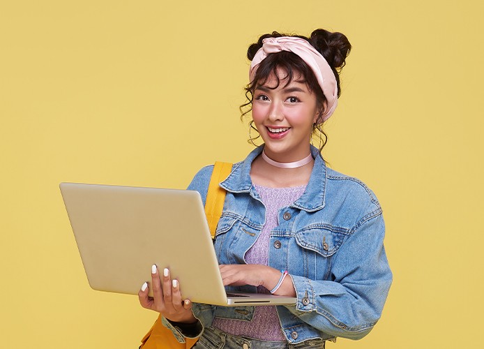 Jonge vrouw houdt een laptop vast en kijkt lachend in de camera.