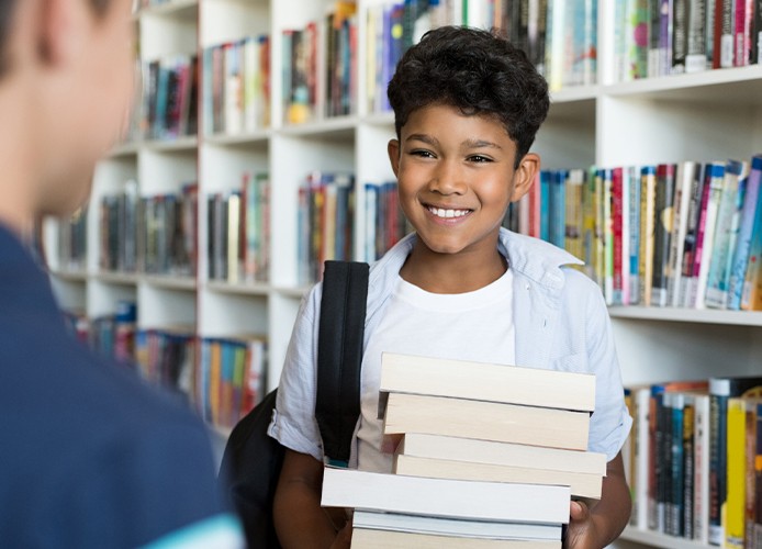 Jongen in de bibliotheek is blij met grote stapel boeken.