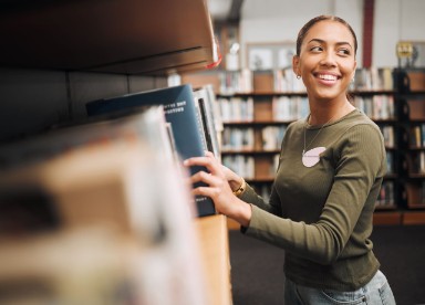 Een vrouwelijke stagiaire van de Bibliotheek West-Brabant ruimt boeken op