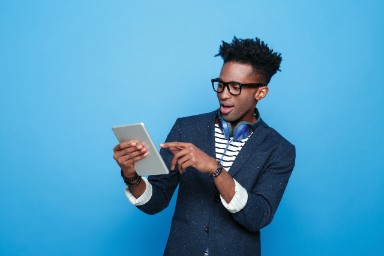 Jonge man met bril staat voor een blauwe achtergrond en wijst enthousiast naar een tablet.